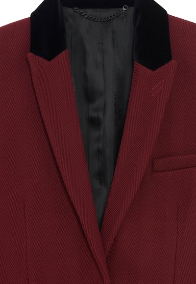 Blazer bordeaux con una texture a spina di pesce, revers in velluto nero e foderato in satin nero. Presenta una tasca sul petto.