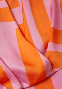 Tissu soyeux en orange et rose avec des rayures audacieuses et lisses. La texture est douce et les couleurs sont vives, créant un motif dynamique.