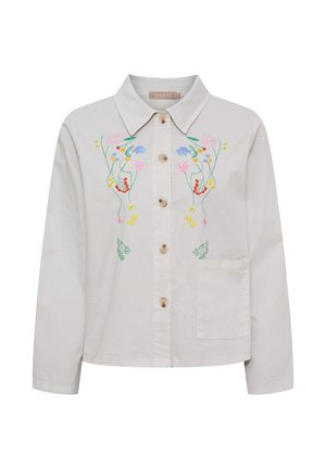 Lyse beige skjorte med knapper og farverig blomsterbroderi på brystet samt en enkelt forlom på højre side.