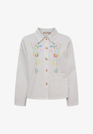 Lyse beige skjorte med knapper og farverig blomsterbroderi på brystet samt en enkelt forlom på højre side.