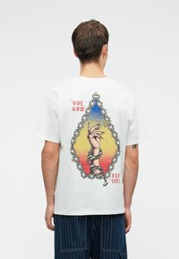 Witte katoenen t-shirt met een kleurrijk grafisch ontwerp op de achterkant, waarop een geketende hand en de teksten "VOLCOM" en "EST 1991" zijn afgebeeld.