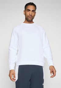 Hvit sweatshirt med rund hals og raglanermer, med en hevet logodetalj. Glatt tekstur og avslappet passform med ribbestrikkede mansjetter.