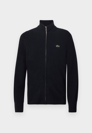 Sweater preto com fecho de correr, gola e punhos canelados, feito de material tricotado. Apresenta um pequeno logótipo verde no lado esquerdo do peito.
