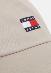 Gorra de béisbol beige con un pequeño parche rectangular del logo de Tommy Jeans en colores rojo, blanco y azul marino en el panel frontal.