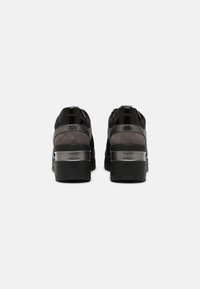 Par av svarta och grå plattformssneakers med metalliska accenter visade från baksidan mot en vit bakgrund.