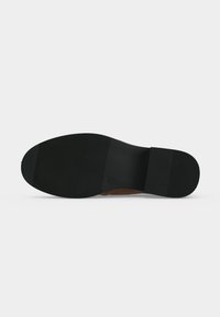 Semelle en caoutchouc noire d'une chaussure habillée avec des motifs texturés antidérapants couvrant le talon et l'avant-pied.