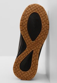 Schwarze Sportschuhsohle mit strukturiertem Grip-Muster, ausgestattet mit einem braunen Gummirand und einem auffälligen Logo.