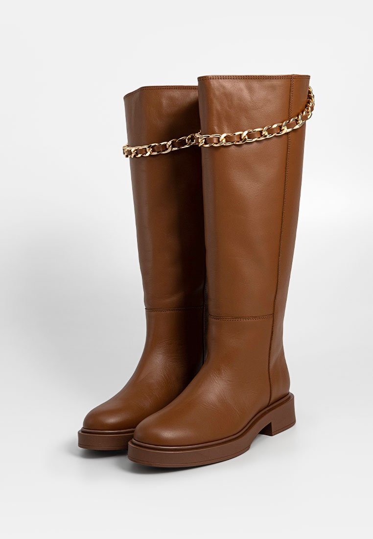 Bruine leren kniehoge laarzen met een platte zool, voorzien van een gouden kettingaccent rond het bovenste gedeelte. Gladde textuur en minimalistisch ontwerp.