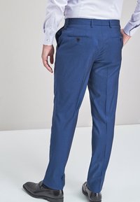 Férfi kék öltöny nadrág, sima textúrával, egyenes szabással, két hátsó zsebbel, gombos záródással, fekete dresszcipővel viselve.