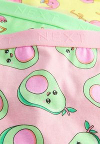Pink stof med tegneserieagtige avocadoer, prydet med grønne og pink detaljer. Elastisk bånd mærket "NEXT" øverst. Lys og legesyg design.