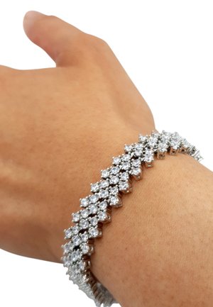 Silbernes Armband mit klaren Strasssteinen in einem Zickzackmuster entlang eines flexiblen Metallbands, das das Licht reflektiert und komplexe Details hervorhebt.
