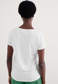 Fehér, rövid ujjú póló, kerek nyakkivágással és laza szabással, könnyű anyagból készült. Simás textúra, látható minták vagy díszítések nélkül.