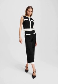 Black textured crop top with white accents and matching black high-waisted pants featuring white pockets, paired with black pointed-toe heels.