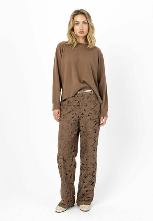 Brązowy sweter z dzianiny z długimi rękawami, zestawiony z luźnymi brązowymi spodniami z motywem kwiatowych wycięć. Spodnie mają pas z paskiem.