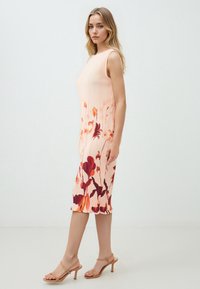 Abito midi plissettato in un delicato pesca con motivi floreali arancioni e bordeaux. Presenta un design senza maniche e un orlo con leggere ruches.