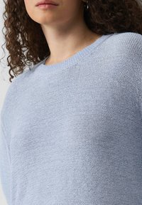 Lichtblauwe gebreide sweater met een ronde hals, textuurstof en een losse pasvorm, toont een close-up van het materiaal en het steekpatroon.