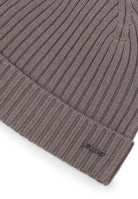 Gebreide muts in lichtbruin met verticale ribbels. Voorzien van een omgeslagen boord en een klein metalen merkembleem aan de zijkant.