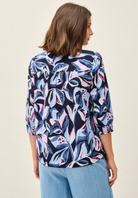 Blusa floreale in blu navy, con motivi di foglie rosa e blu, maniche a tre quarti con polsini arricciati e vestibilità comoda.