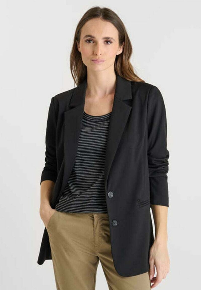 Blazer noir avec un revers classique et des manches longues, comportant deux boutons et une poche. Porté sur un haut rayé et un pantalon beige.