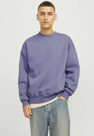 Paarse sweatshirt met een ronde halslijn, geribbelde boorden en onderrand. Draagt over een lichtgekleurde onderhemd, gecombineerd met lichtblauwe jeans.