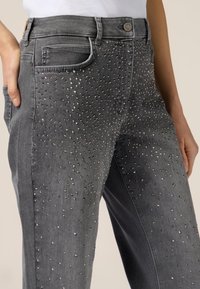Jeans in denim grigio con design aderente, impreziositi da borchie metalliche disposte in un motivo a pois lungo la parte frontale.
