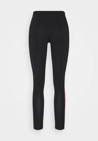 Svarta tajta leggings med hög midja och smal röd rand som löper längs utsidan av varje ben.