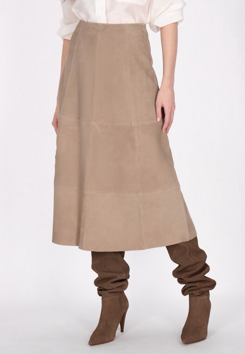 Beige ruskind midi-nederdel med paneldesign, høj talje og A-linje form. Sammenstillet med brune, slouchy hæl-støvler for kontrast.