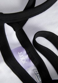 Zwarte elastische banden op een witte stof met een ribbelstructuur. Het label toont "JUXX" en geeft maat S aan, gemaakt in Bangladesh.