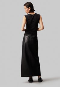 Top senza maniche nero abbinato a una lunga gonna in pelle nera con tasche posteriori e una texture liscia. Le calzature sono scarpe nere con suola spessa.