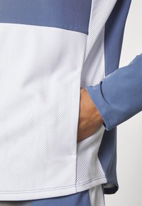 Sport top made of breathable mesh and smooth fabric. Color gradient from light to dark blue, with a side pocket for convenience.