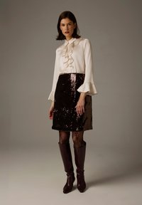 White blouse with ruffled collar, paired with a sequined brown skirt. The model wears black fishnet tights and brown knee-high boots.