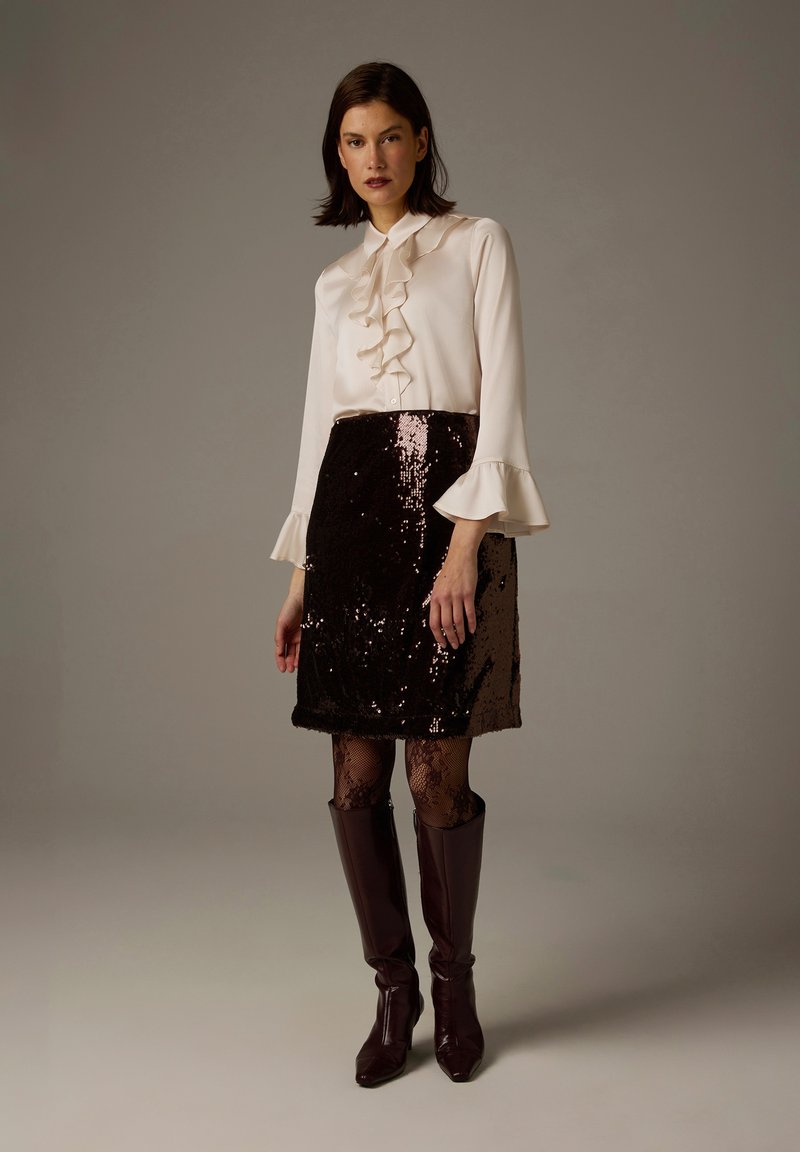 White blouse with ruffled collar, paired with a sequined brown skirt. The model wears black fishnet tights and brown knee-high boots.