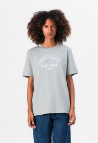 T-shirt en coton gris à manches courtes, arborant le texte "TOMMY JEANS NEW YORK" imprimé en blanc et violet. Coupe décontractée, col rond.