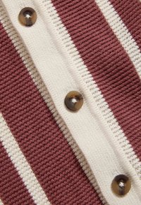 Pletený kardigan s bordovými a krémovými horizontálními pruhy, velkými hnědými knoflíky a strukturovanou tkaninou.