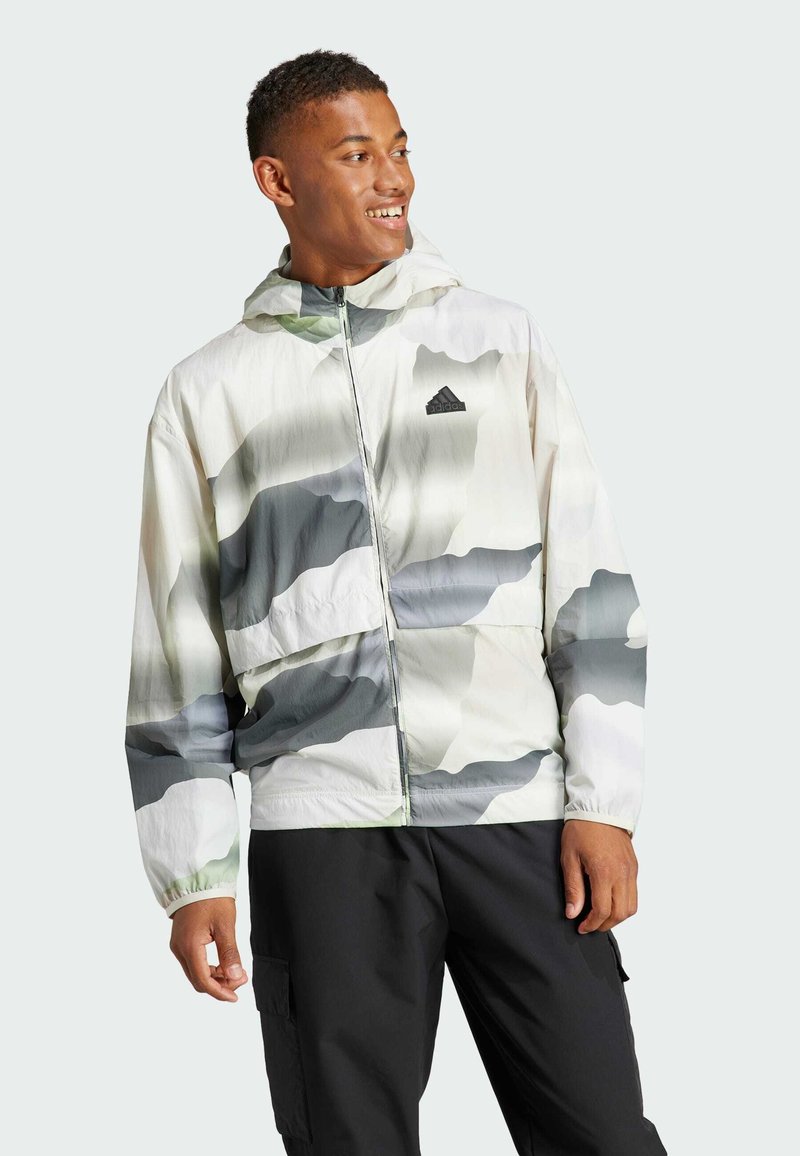 Lightweight hooded jacket in a green and gray abstract camouflage pattern, with a zip front and elastic cuffs. Black logo on chest.