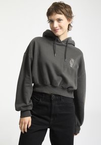 Donkergrijs cropped hoodie met een voorste kangoeroezak, capuchon met trekkoord en geborduurd ontwerp. Gecombineerd met zwarte high-waisted jeans.