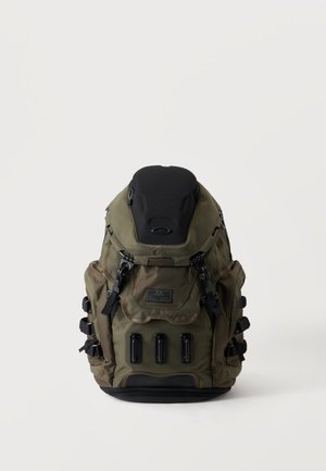 Sac à dos vert militaire et noir avec plusieurs compartiments, bretelles réglables et trois points de ventilation ou d'attache noirs sur la partie inférieure avant.