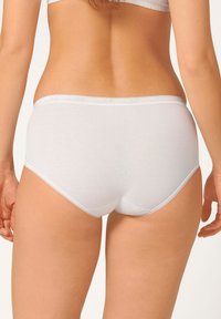 Slip hipster bianco in cotone con una texture liscia e elastica, dotato di un bordo decorativo in pizzo lungo l'elastico in vita e le aperture delle gambe.