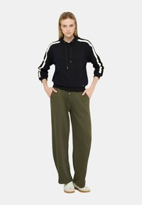 Felpa con cappuccio blu navy con dettagli a striscia bianca a contrasto, abbinata a pantaloni larghi verde oliva e sneaker bianche.