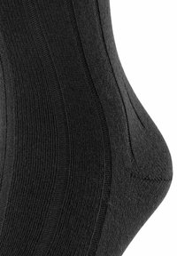 Sort bomuldsstrømpe med ribbet struktur, en aftagende form og en glat finish, med subtile variationer i strikmønstret.