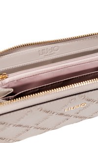 Portafoglio rosa chiaro con zip dorata, dotato di un vano interno e foderato in beige. Il nome del marchio "LIU-JO" è visibile.