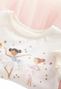 Cremefarbenes Baumwoll-T-Shirt mit kurzen, rüschengeschnittenen Ärmeln, das ein zartes Ballett-Motiv und pastellfarbene Tüll- Akzente zeigt. Der Hintergrund besteht aus zartem rosa Tüll.