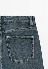 Achteraanzicht van een blauwe spijkerbroek met één achterzak, zichtbare stiksels en lussen voor een riem op een witte achtergrond.