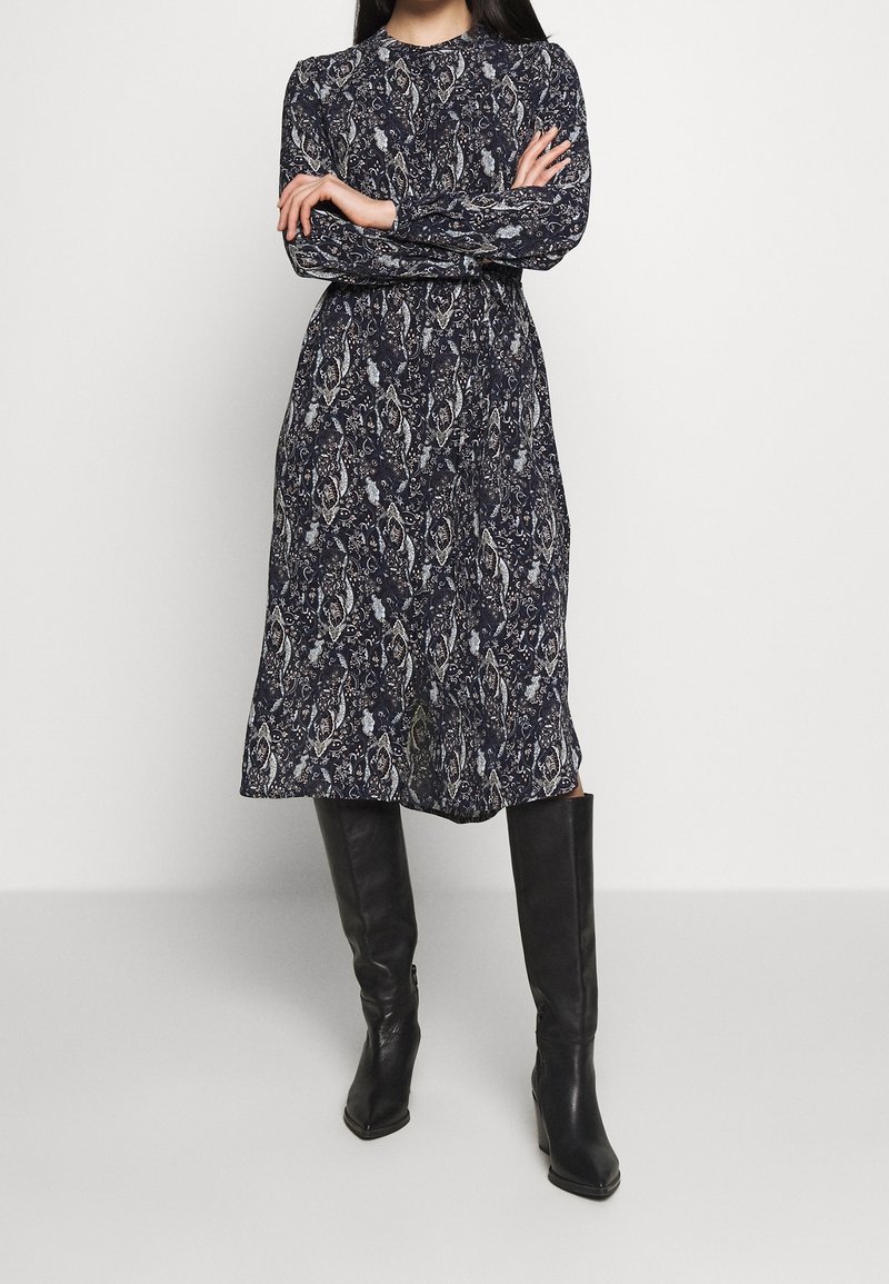 Sukienka midi w marynarskim wzorze z długim rękawem, okrągłym dekoltem i kwiatowym wzorem; zestawiona z czarnymi botkami do kolan.