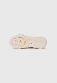 Semelle de chaussure en beige clair avec un caoutchouc texturé pour une meilleure adhérence. Présente un motif de crampons prononcé et un accent logo jaune.