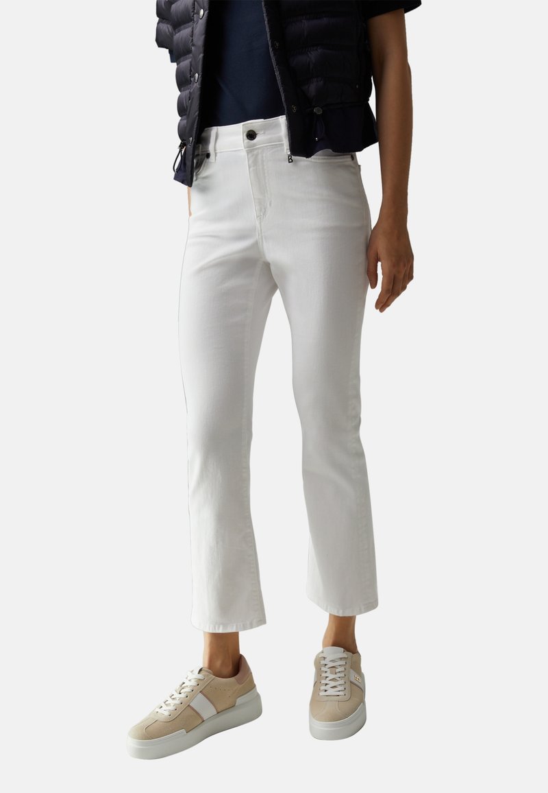 Jean blanc court à la coupe ajustée, associé à des baskets basses beige et blanches. La tenue comprend une veste matelassée foncée et un haut bleu marine.