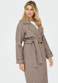Beige bælte trenchcoat med kiggerkrave, dobbeltradet front og lange ærmer. Stoffet ser tekstureret og blødt ud.