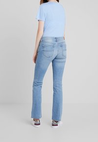 Jeans de mezclilla azul claro con pata de elefante, de cintura media y con bolsillos traseros, combinados con una camiseta azul claro y zapatillas blancas.