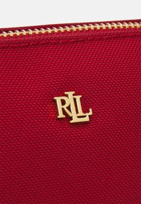 Czerwona torba materiałowa o teksturowanym wykończeniu, z złotym logo RL i złotym suwakem u góry.