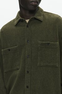 Groene button-up shirt van een gestructureerde stof, met twee borstzakken en zwarte knopen. Subtiele merkaccent op de zakzijde.